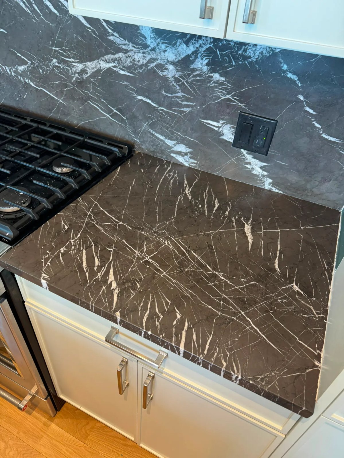 Dark marble countertop and backsplash with white veining in a modern kitchen.