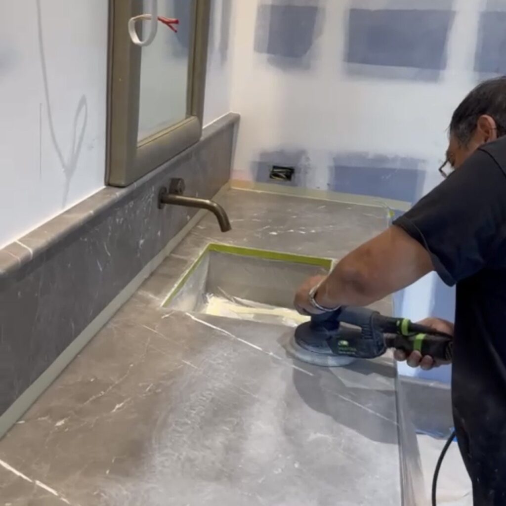Technician polishing a gray marble vanity with an orbital tool.