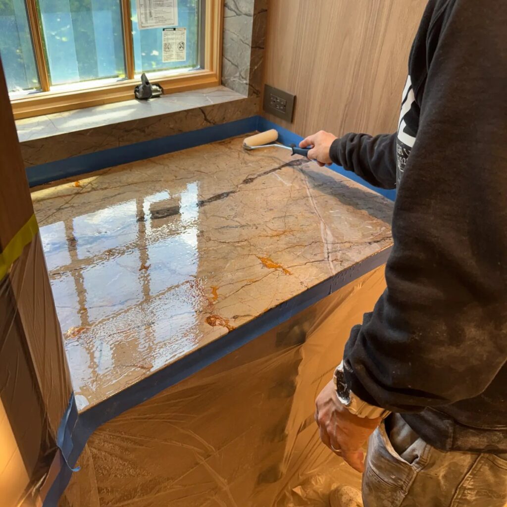 Technician applying a protective coating to a marble countertop with a roller.