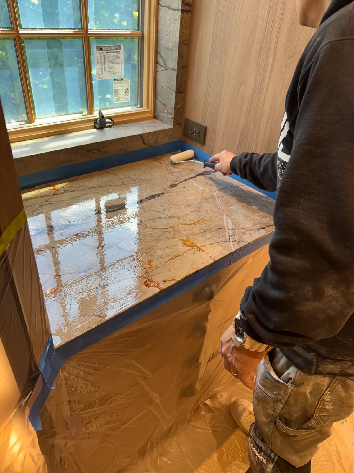 Technician applying a protective coating to a marble countertop with a roller.